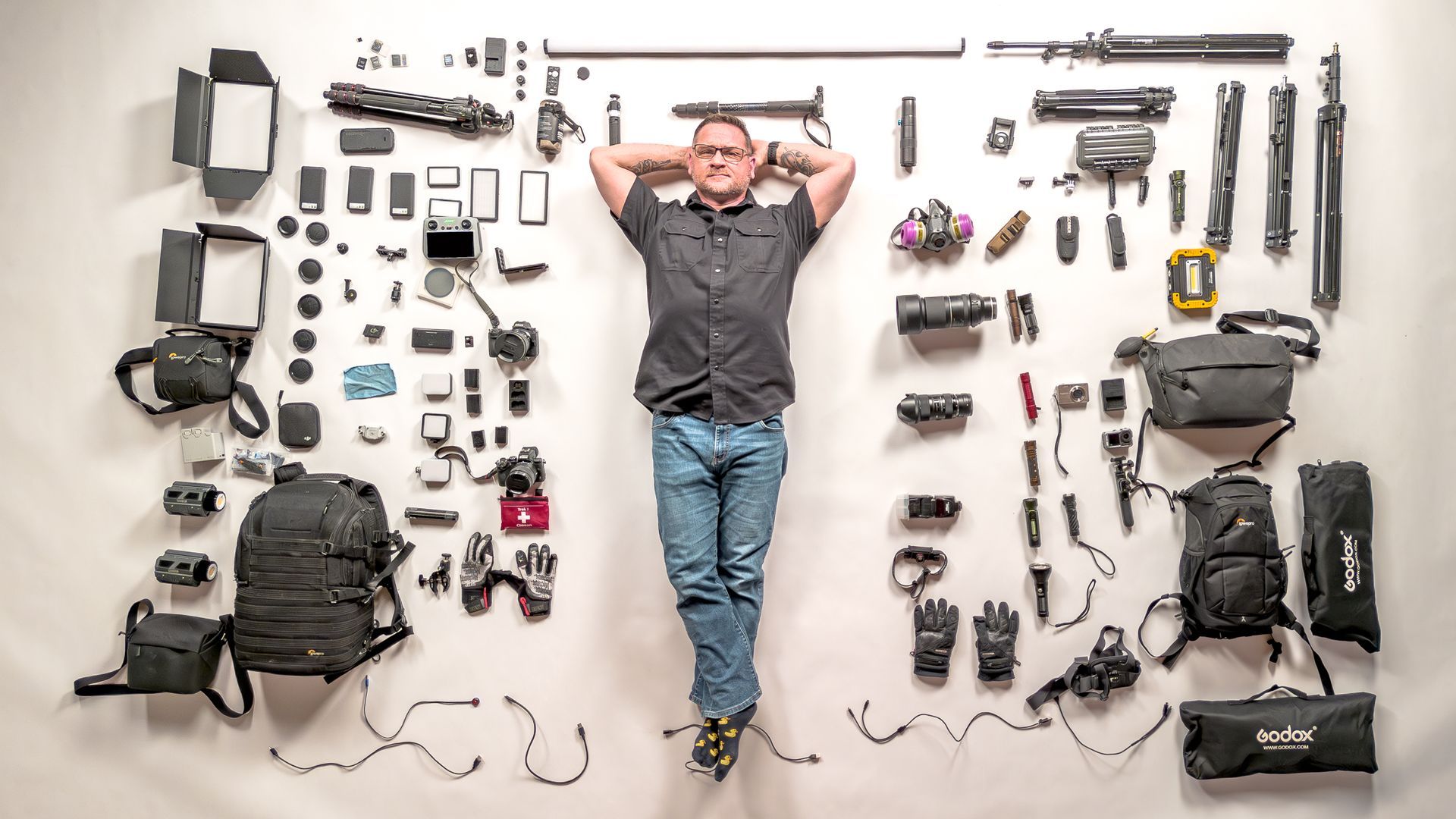 Man lying on white background surrounded by photography and urban exploration gear
