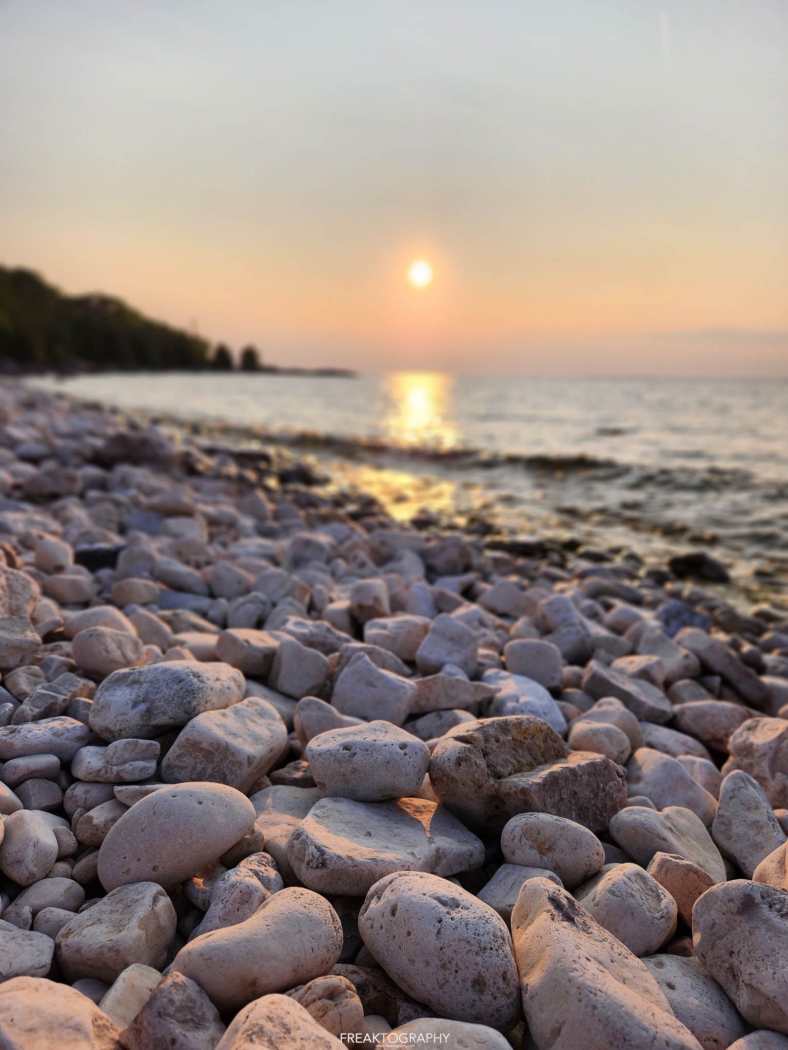 A pile of rocks on a beach with the sun setting in the background.