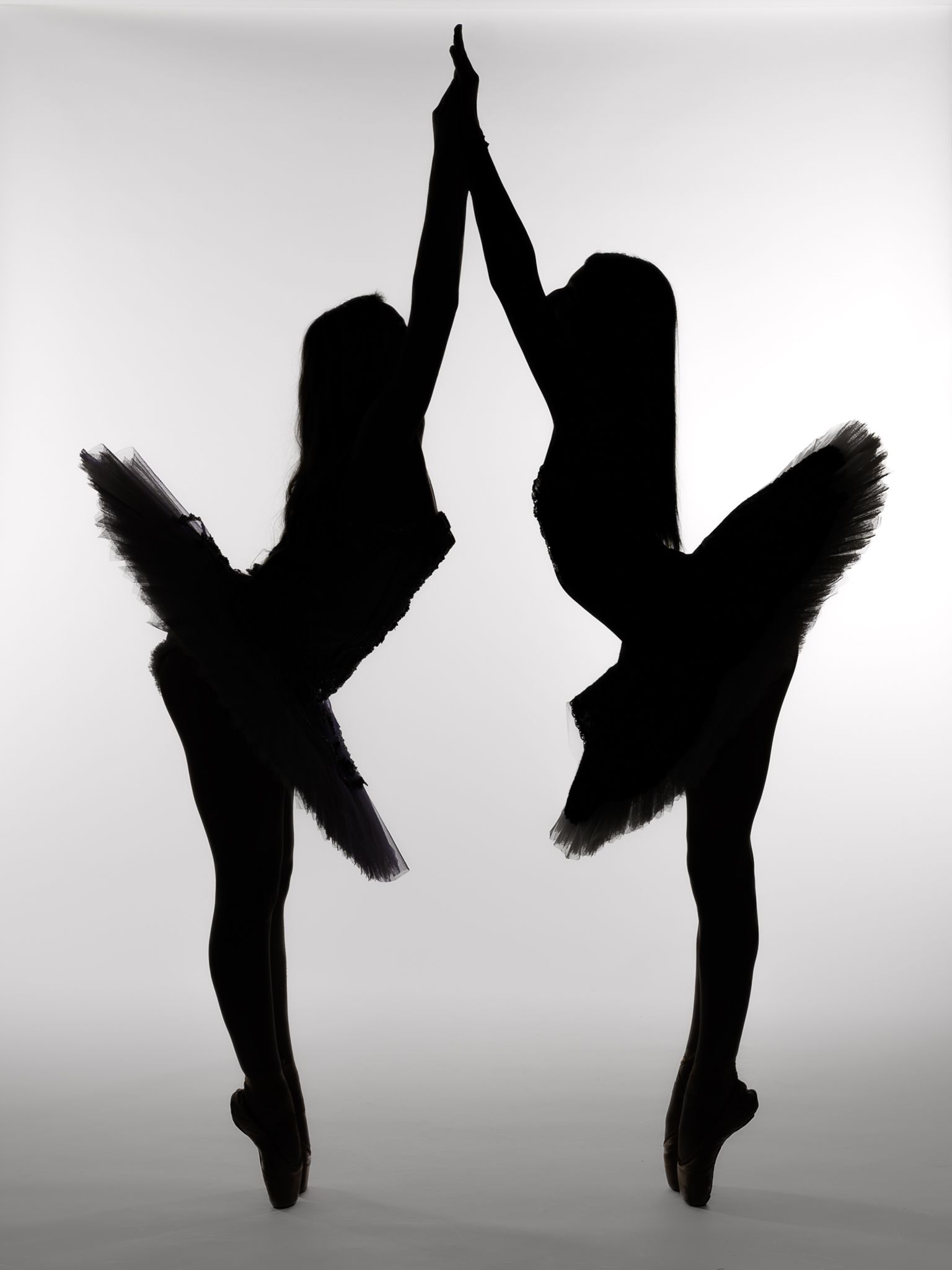 Silhouette of two ballerinas in tutus balancing on pointe with arms extended upward and touching