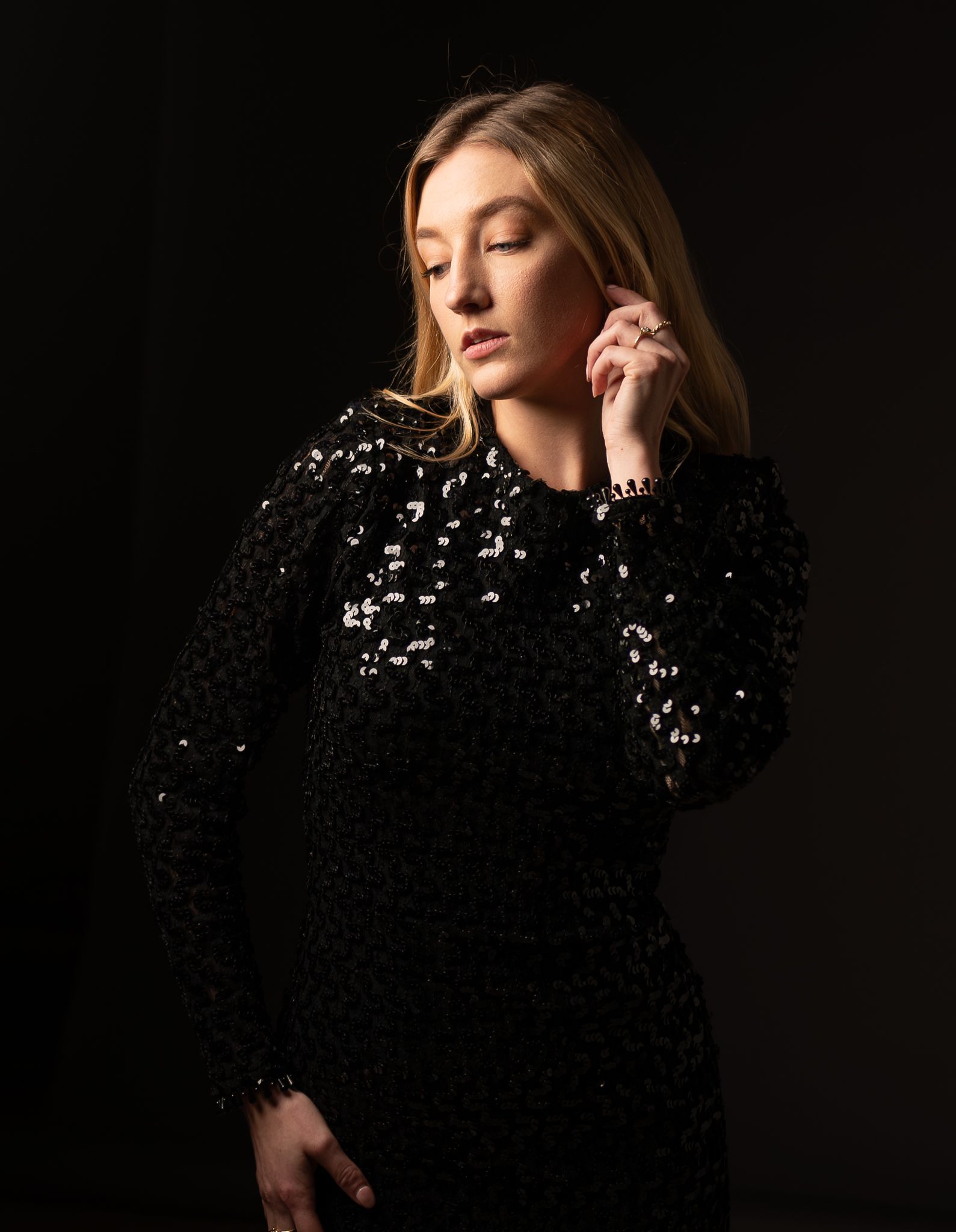 Portrait of Sarah Van Der Valk in a black sequin dress, softly lit in a studio against a dark background