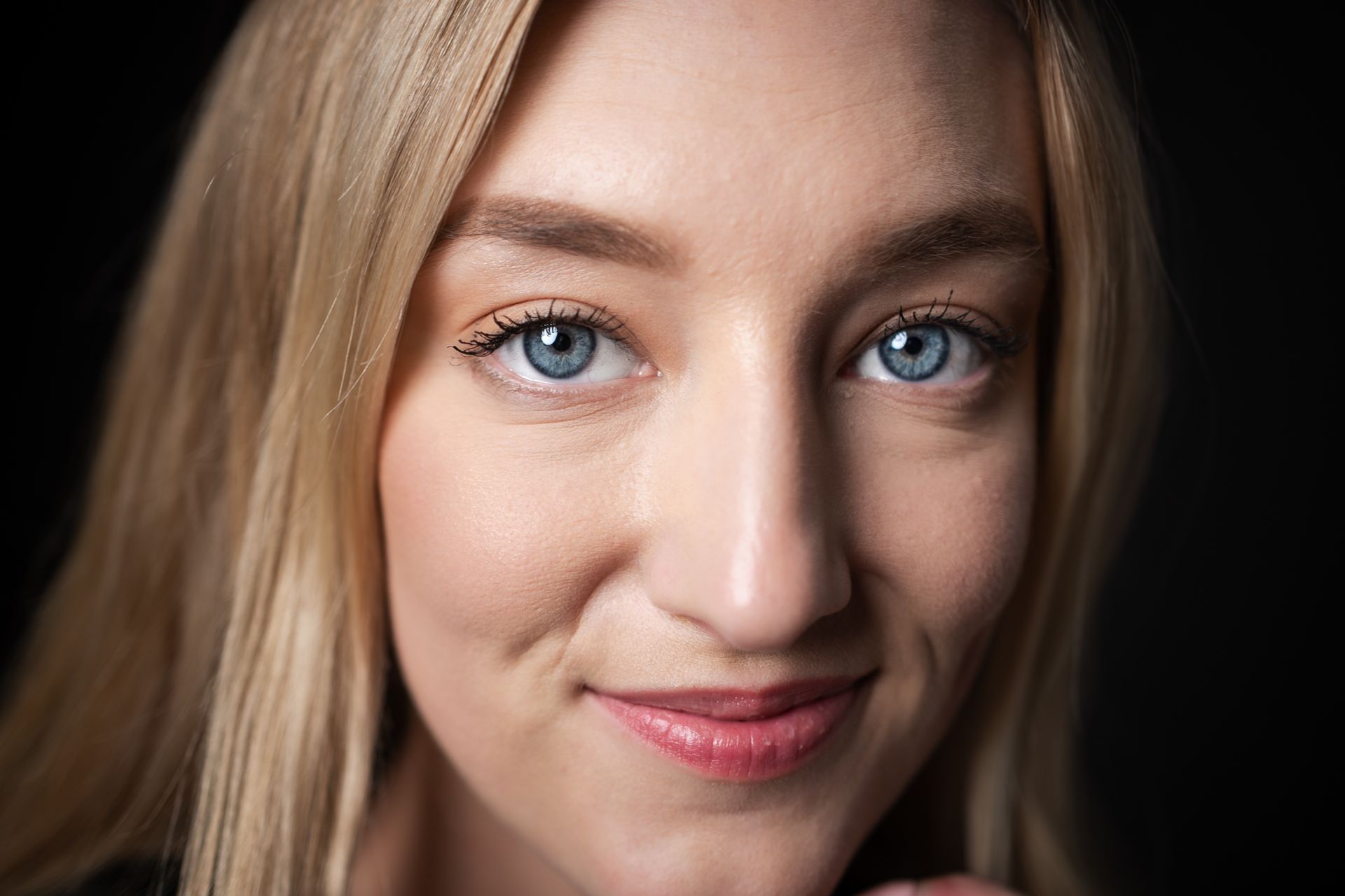 Close-up portrait of a smiling woman with blue eyes and blonde hair against a black background