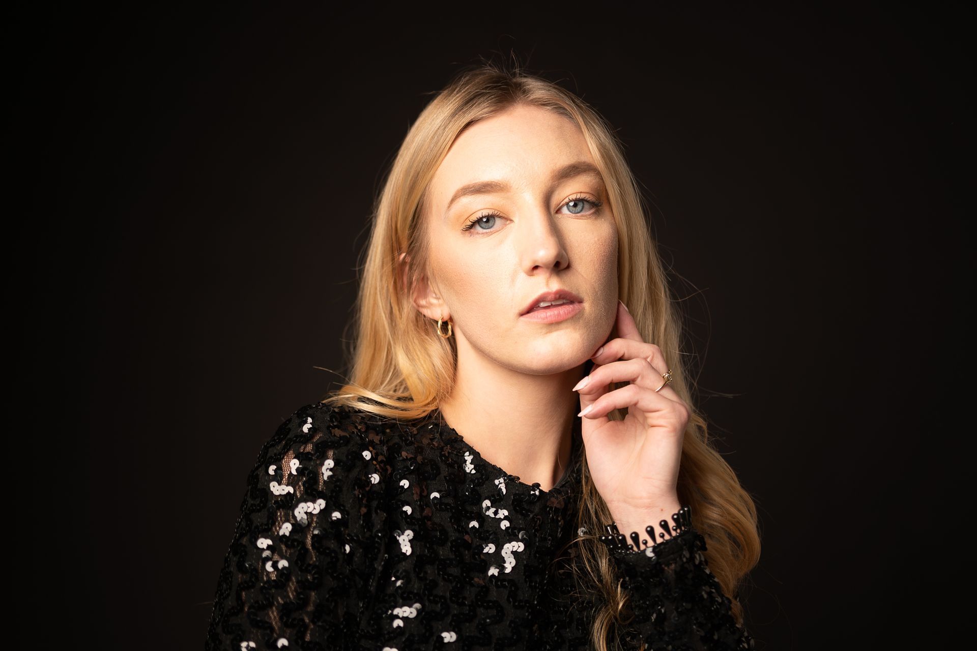Portrait of Sarah Van Der Valk in a black sequin dress, softly lit in a studio against a dark background
