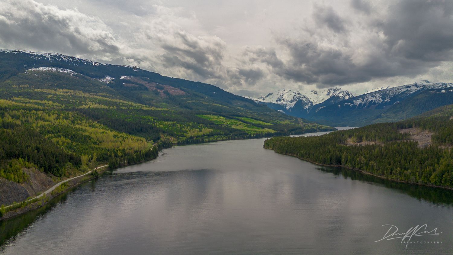 An aerial view of a lake surrounded by mountains on a cloudy day.