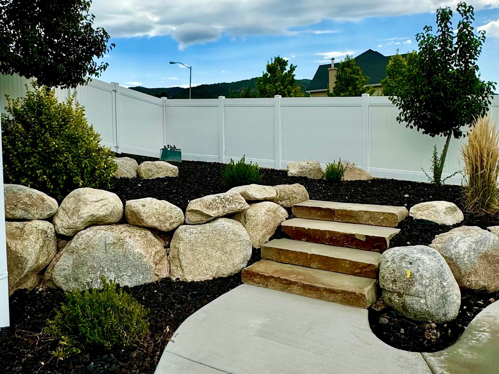 A white fence is surrounded by rocks and steps in a garden.