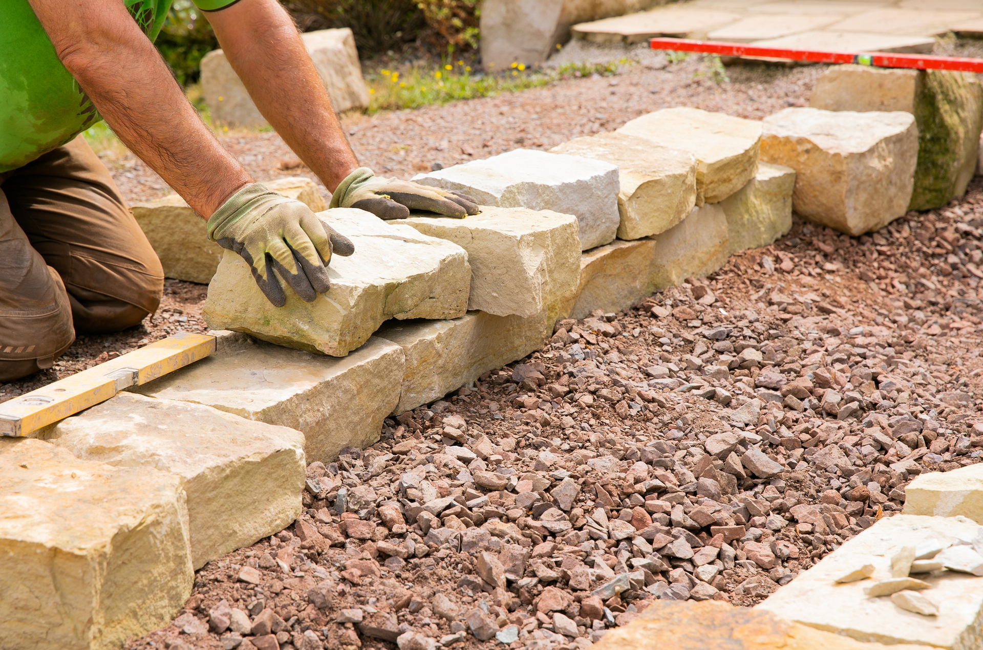 A man is laying rocks on top of gravel in a garden.
