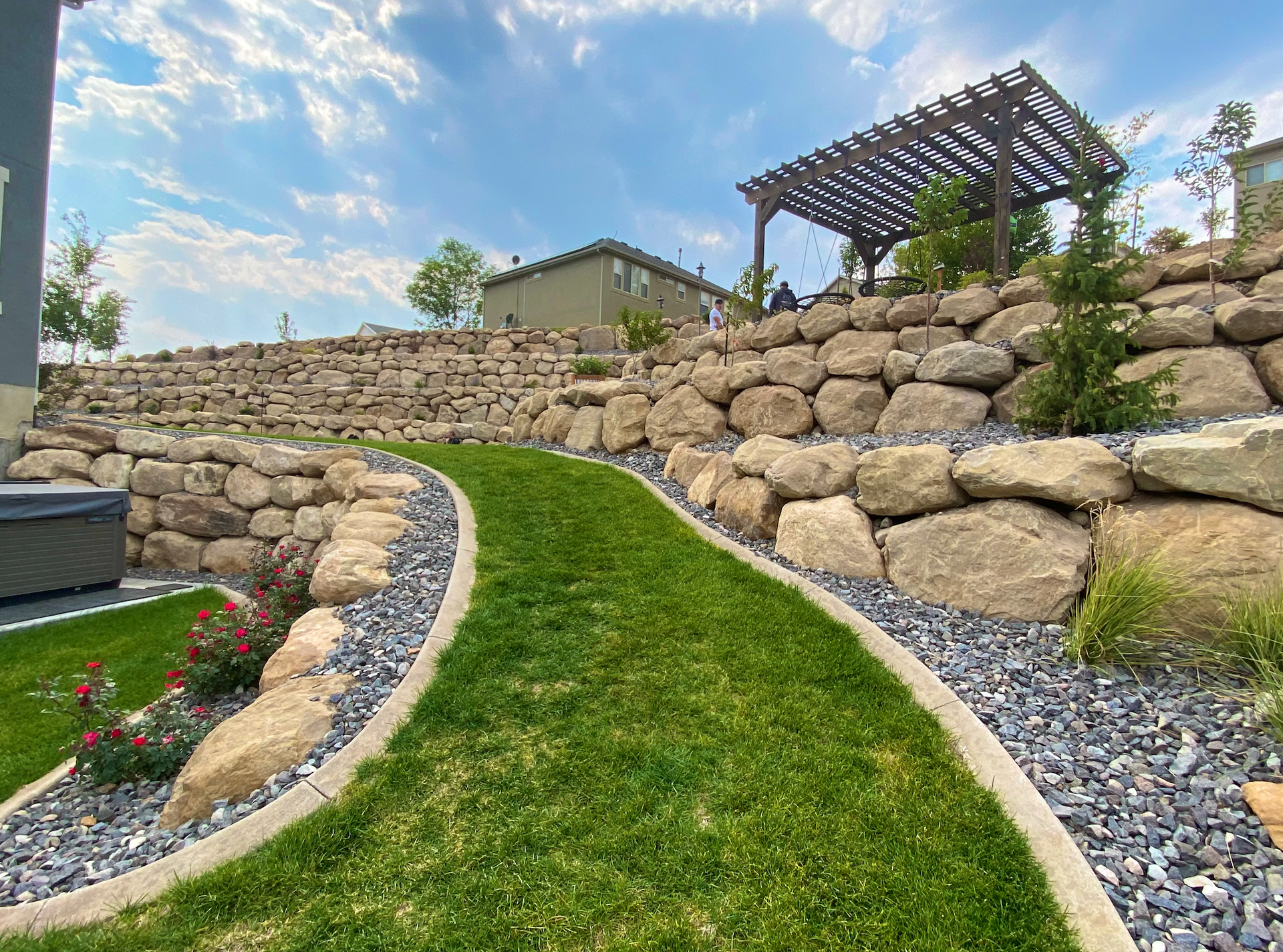 A stone wall surrounds a lush green lawn in a backyard.