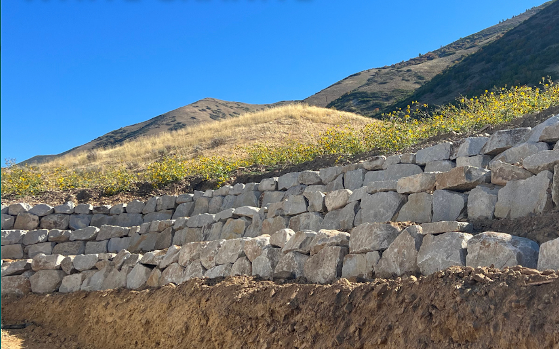 A stone wall on a hillside with mountains in the background