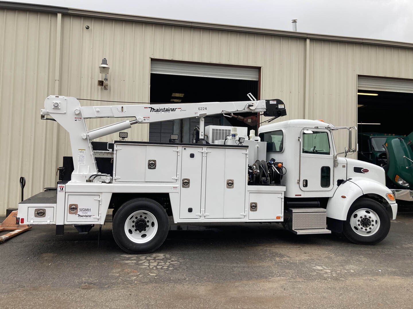 A white truck with a crane on the back is parked in front of a building.