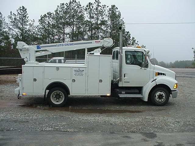 A white utility truck is parked in a gravel lot