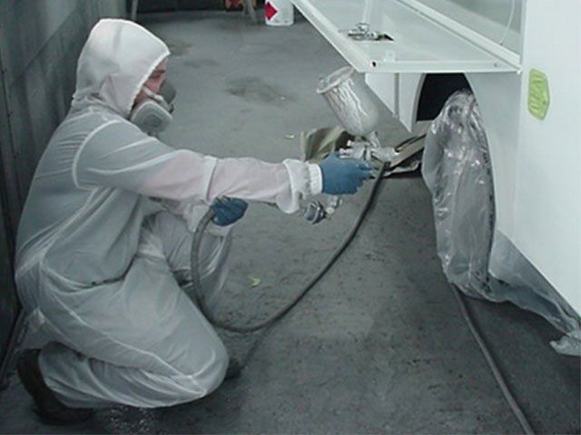 A man in a protective suit is spraying paint on a vehicle
