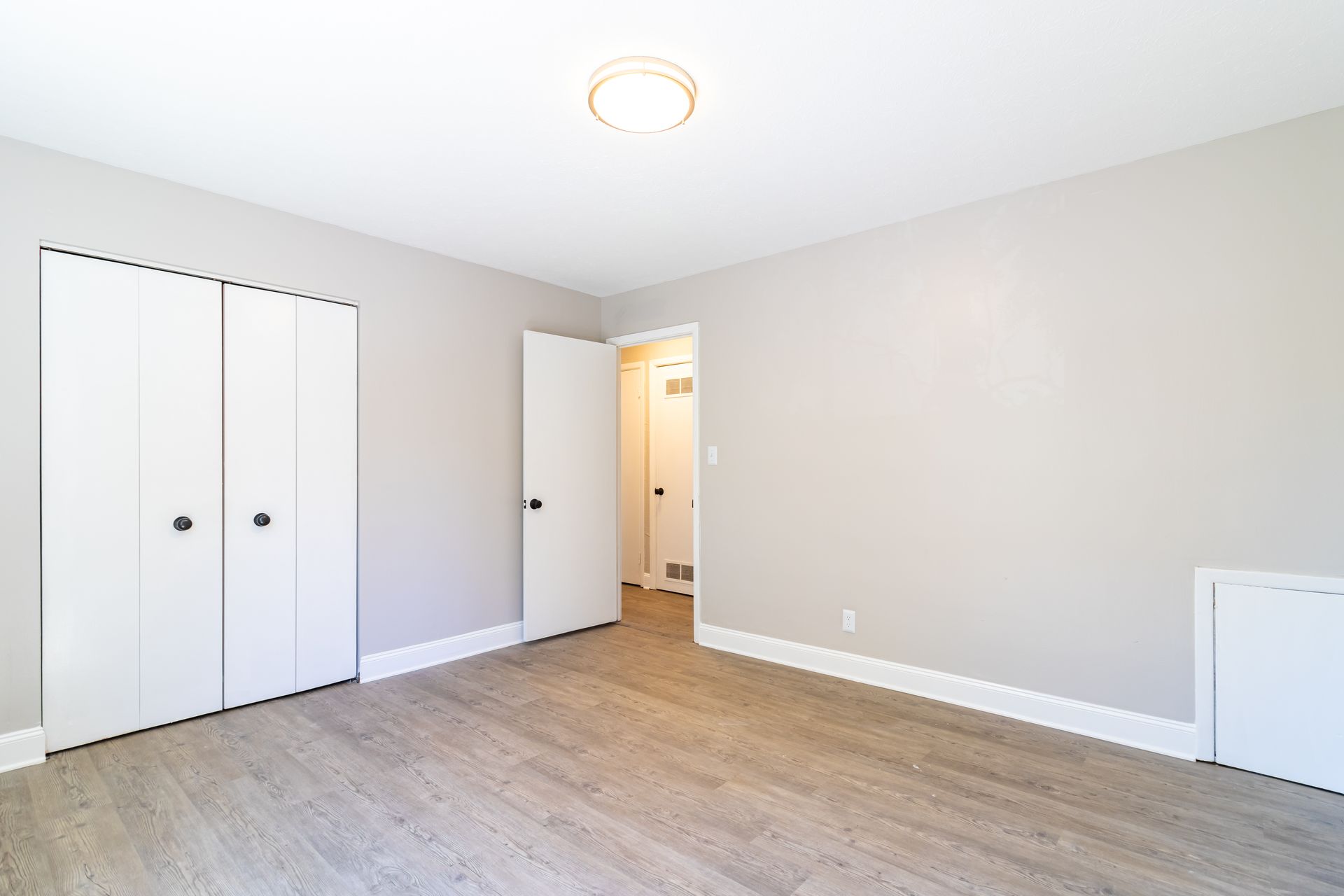 An empty bedroom with hardwood floors and white walls.