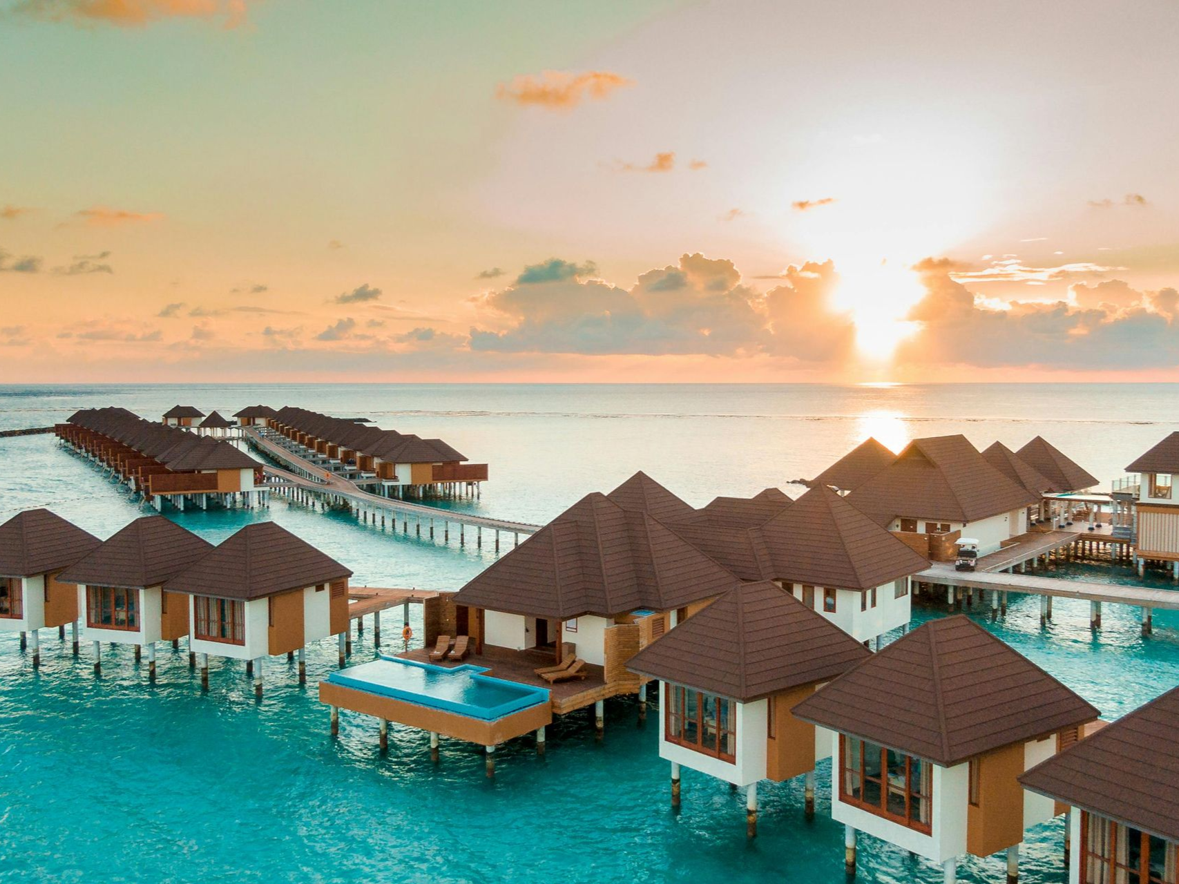 Overwater bungalows at sunset, turquoise water, golden sky, wooden walkways.
