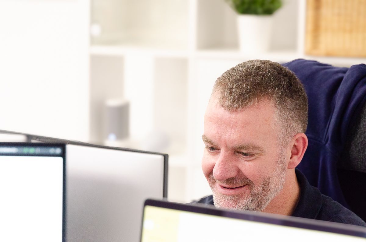 A woman is smiling while sitting at a desk in front of a computer.