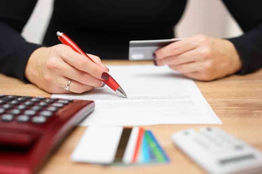 A woman is holding a credit card and writing on a piece of paper.