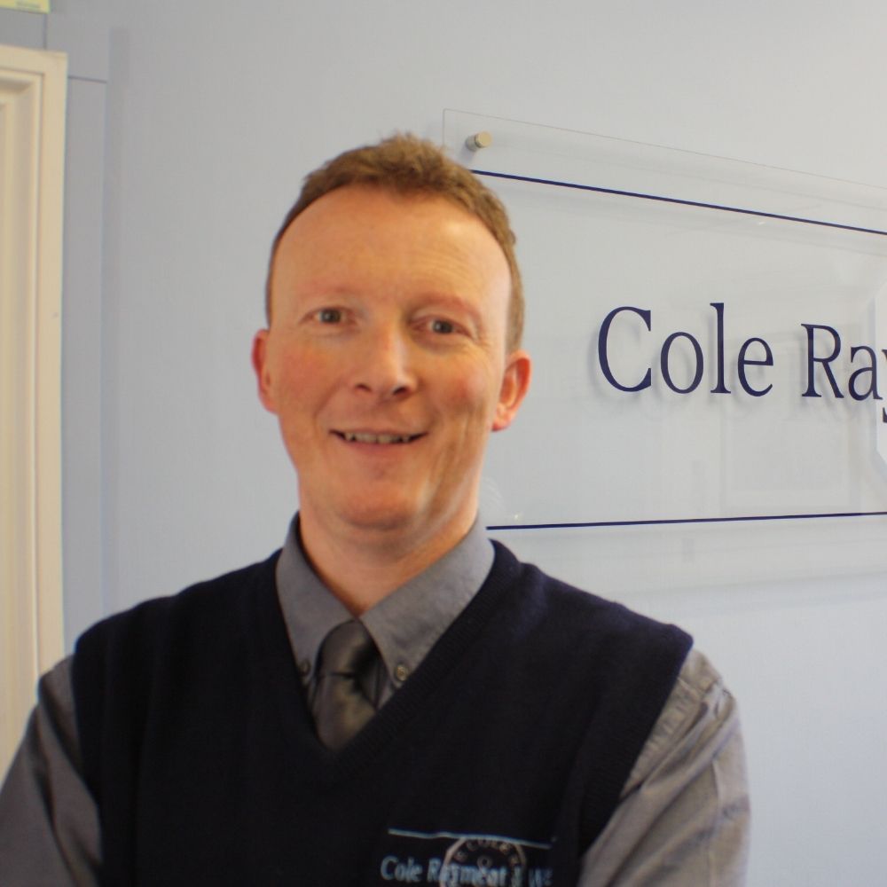 A man standing in front of a sign that says Cole, Rayment and White