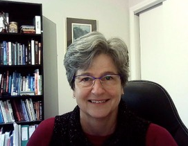 A woman wearing glasses is smiling in front of a bookshelf