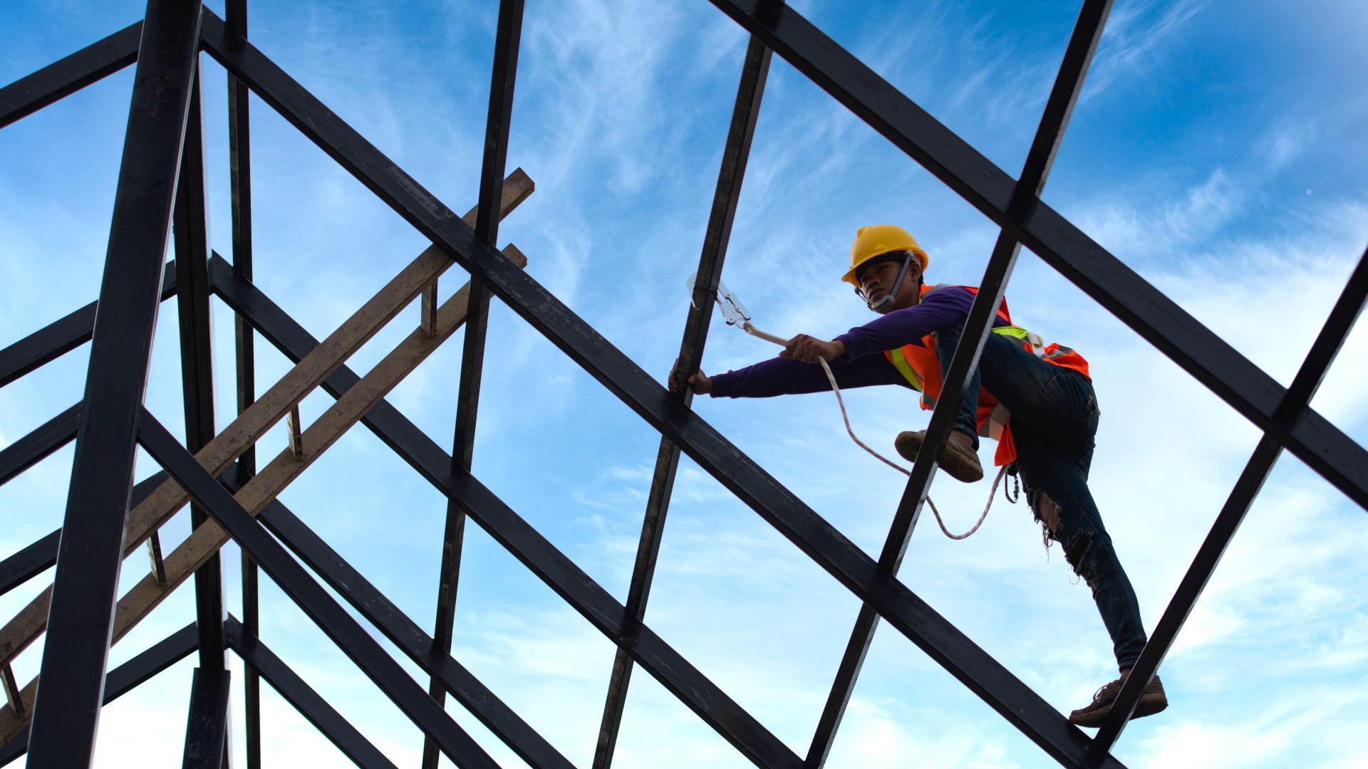 A construction worker is climbing up a metal structure.