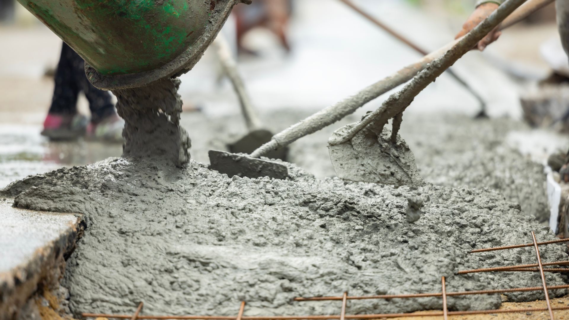 A person is pouring concrete on a sidewalk with a shovel.