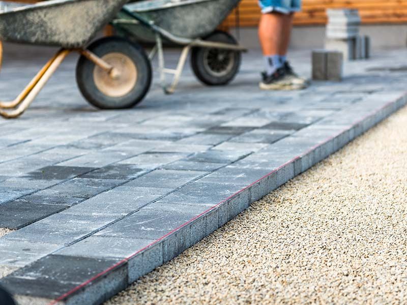 A man is pushing a wheelbarrow on a brick driveway.