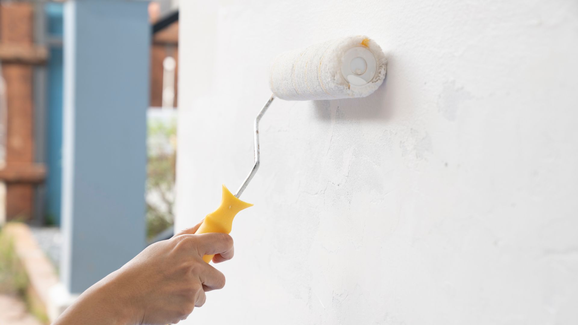 A person is painting a wall with a paint roller.