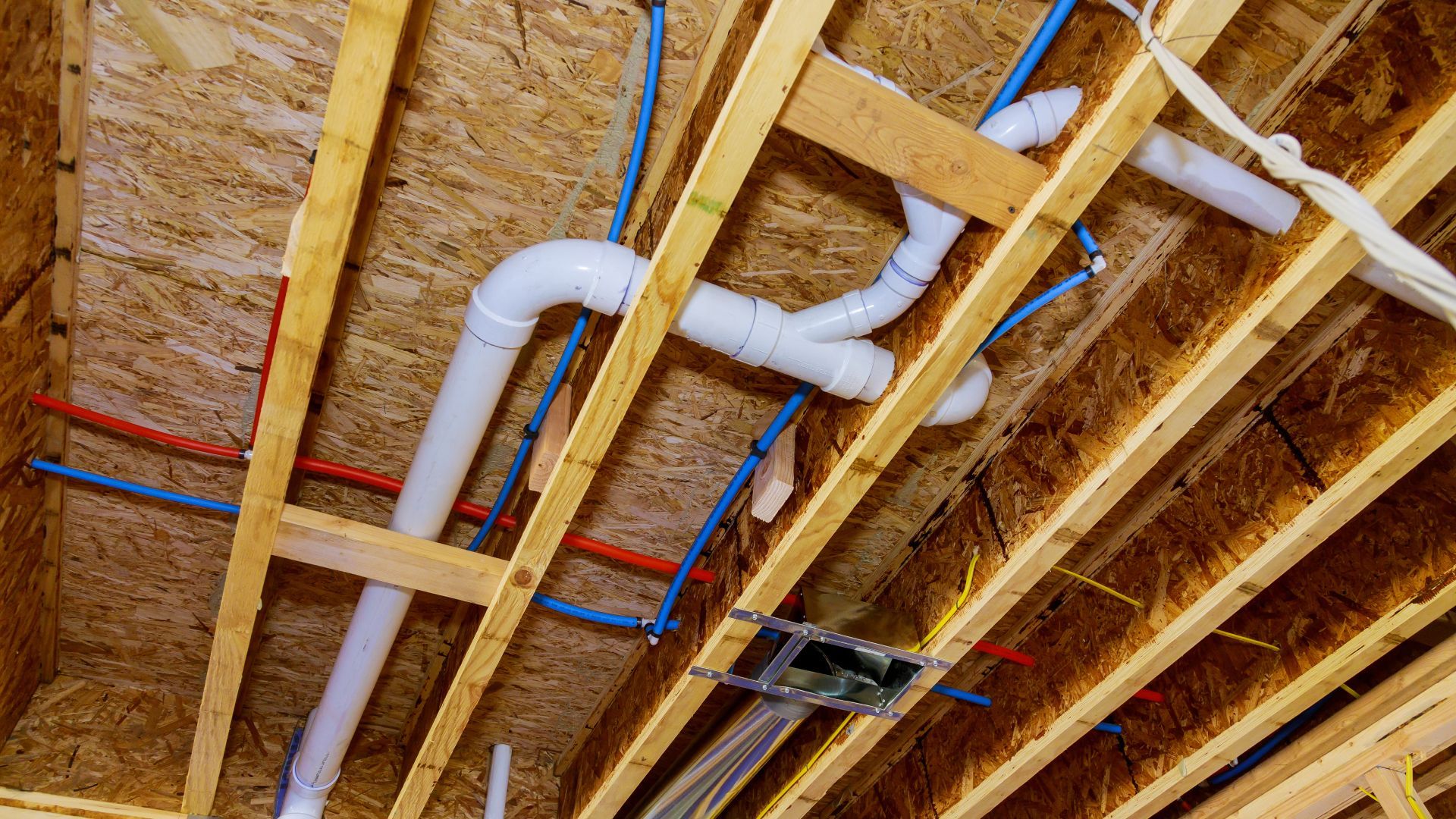 A house under construction with pipes and wires coming out of the ceiling.