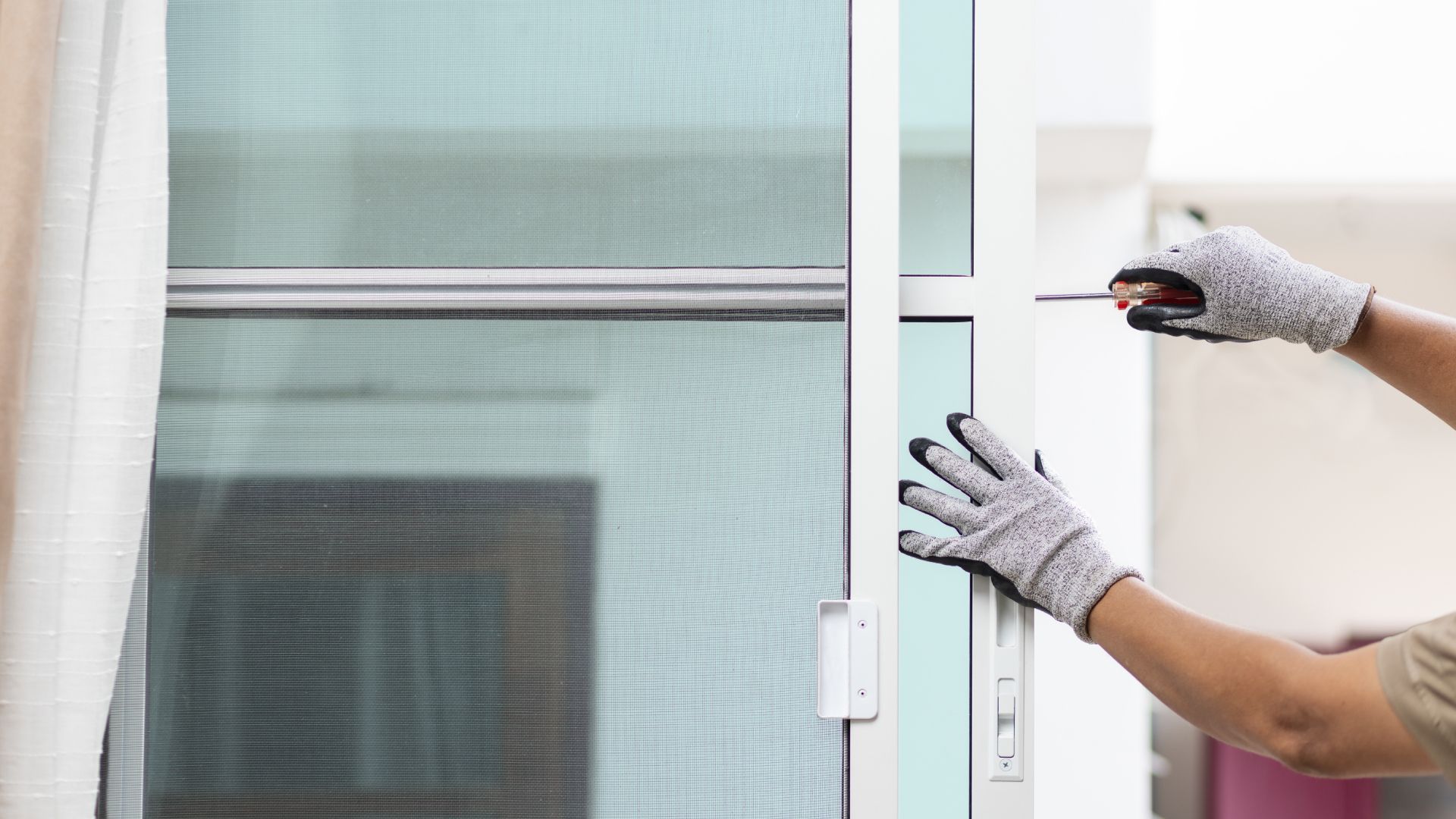 A person is opening a screen door with a screwdriver.