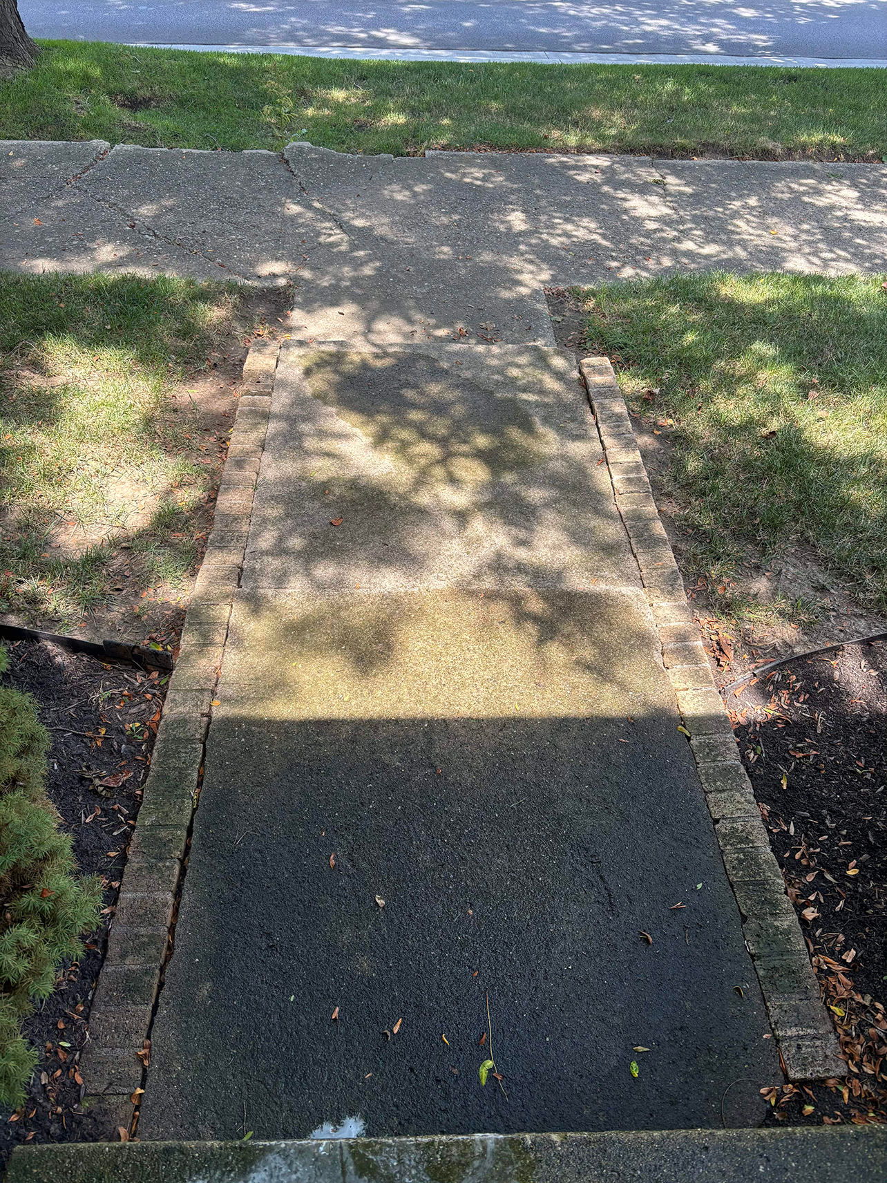 Concrete sidewalk leading to a darker, brick-edged landing with shadows cast across it.