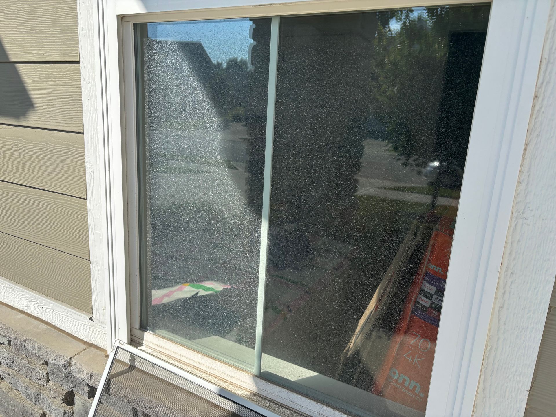 Sliding glass door with condensation, partially reflecting a yard and house exterior.
