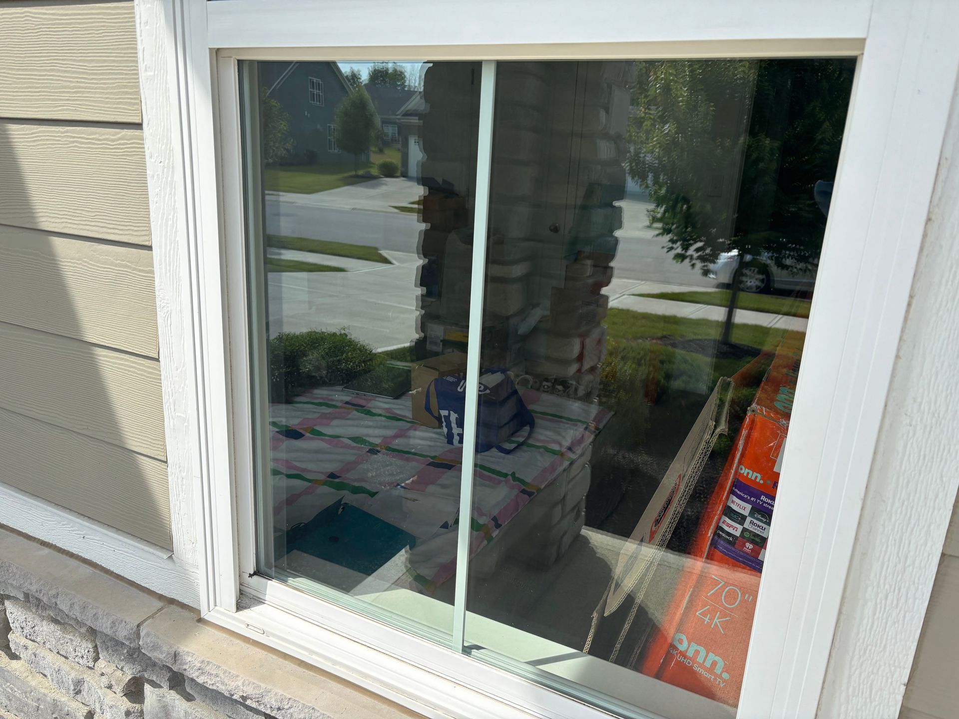 White-framed window reflecting a sunny outdoor scene, including a brick pillar and nearby street with a car.