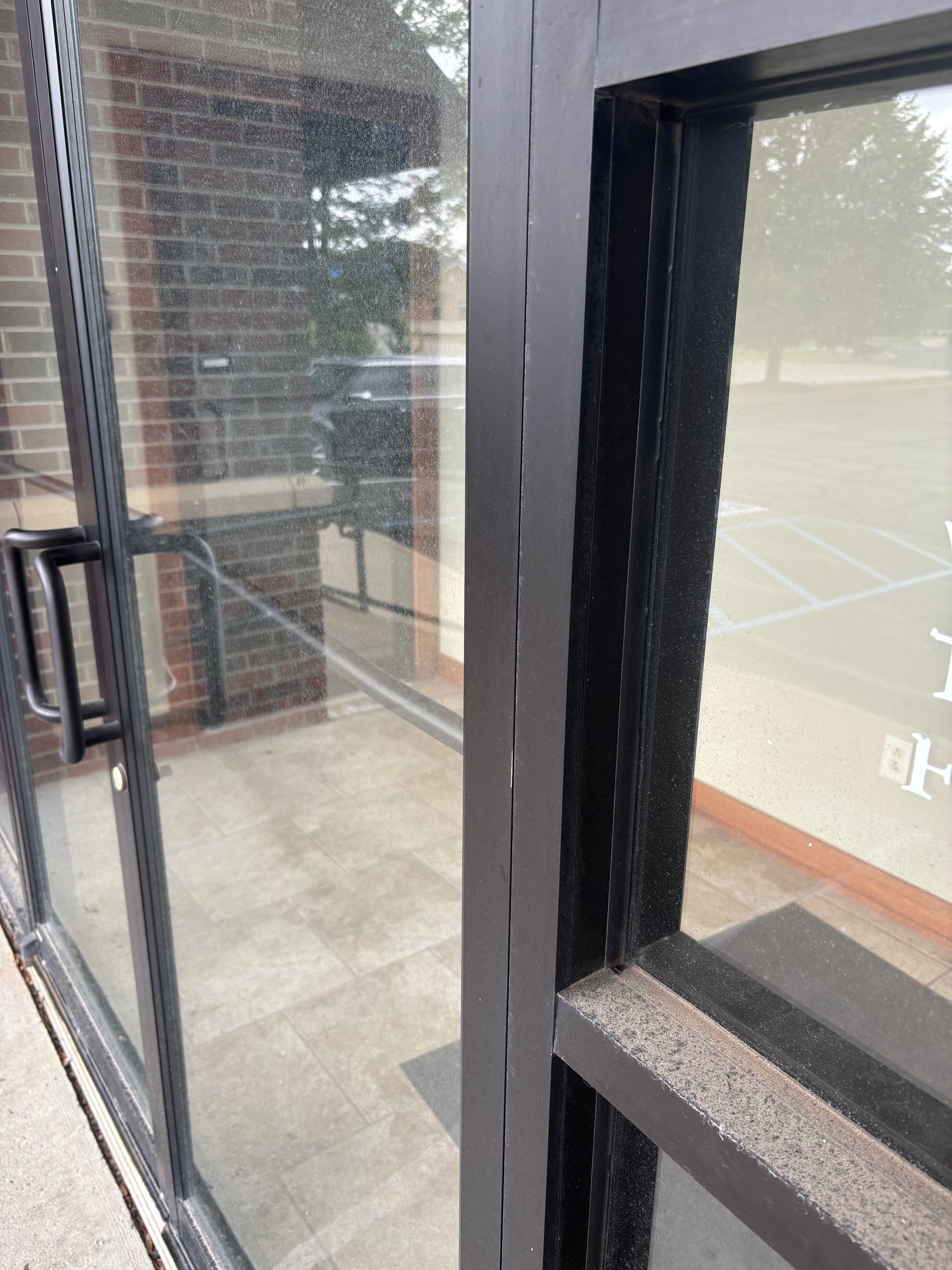 Exterior of building with glass doors and windows, black frames, brick wall visible.