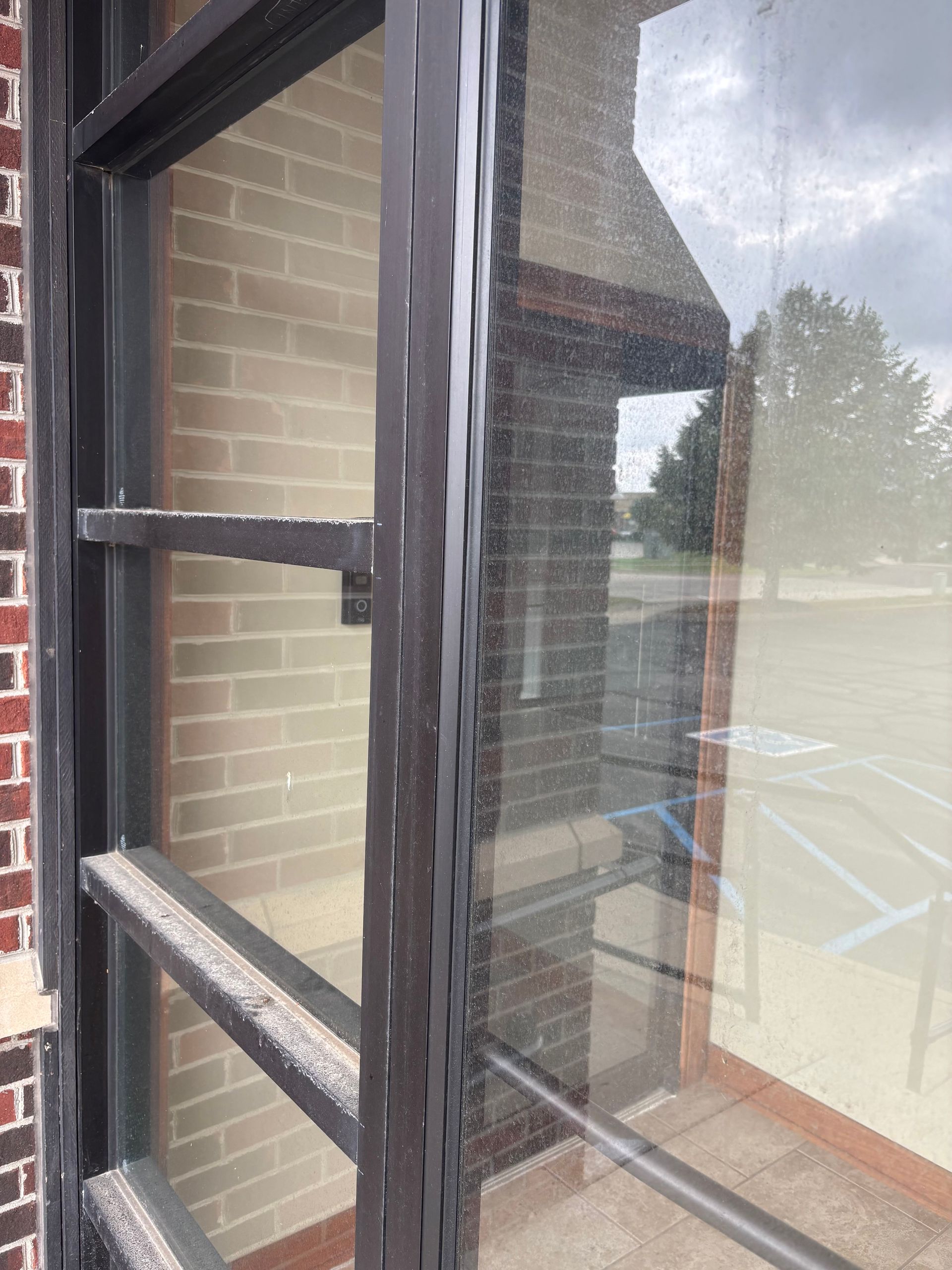 A window with black frames against a brick wall, reflecting a building and a playground.