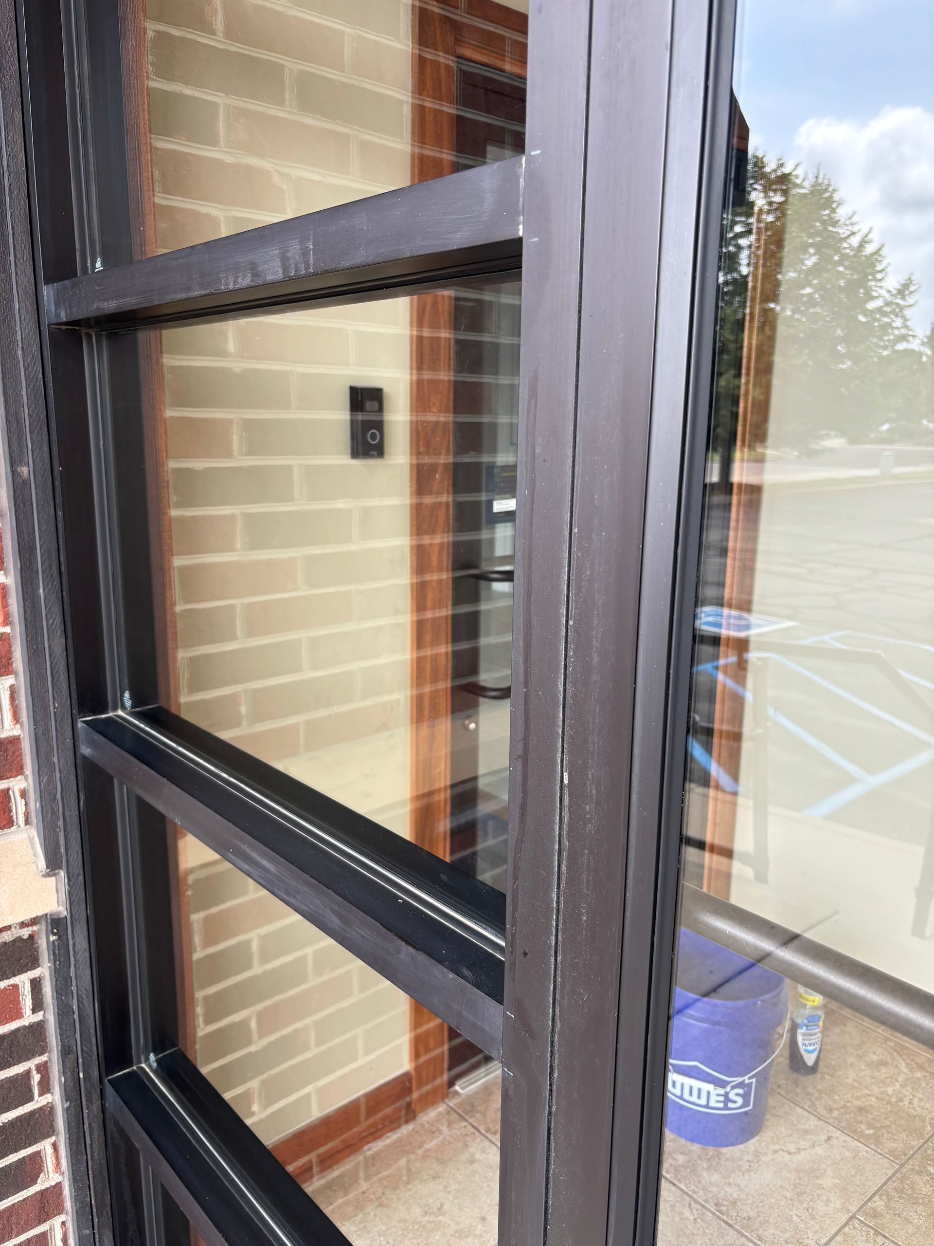 Exterior brown door frame with glass, reflecting a brick wall and a parking lot.