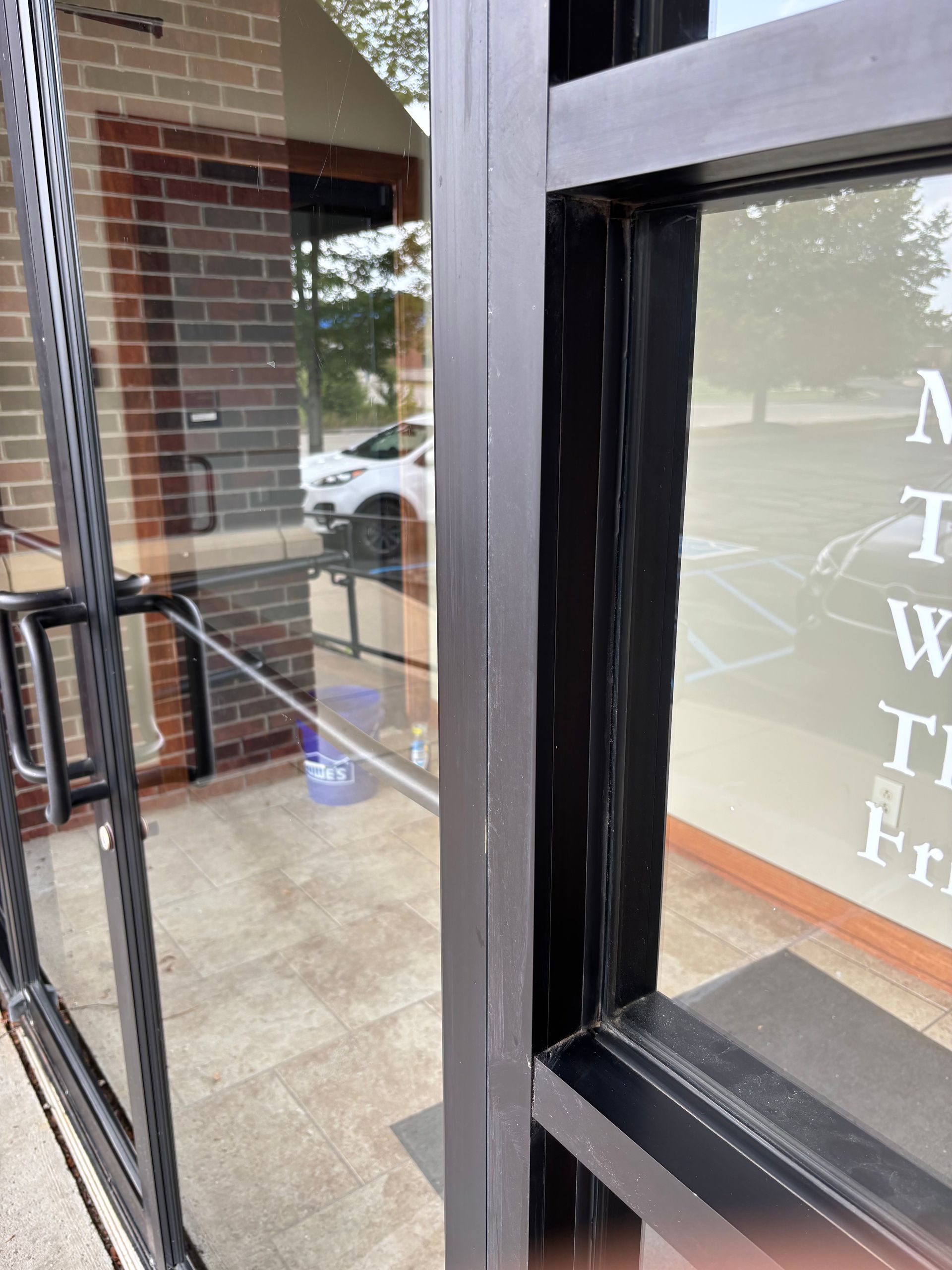 Exterior door and window frame of a commercial building; brick wall visible through glass.
