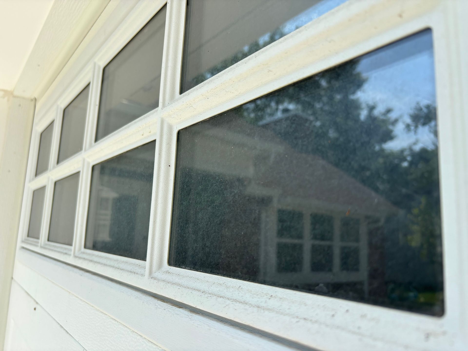 White-framed window with multiple panes reflecting a building and trees, set in a white wall.