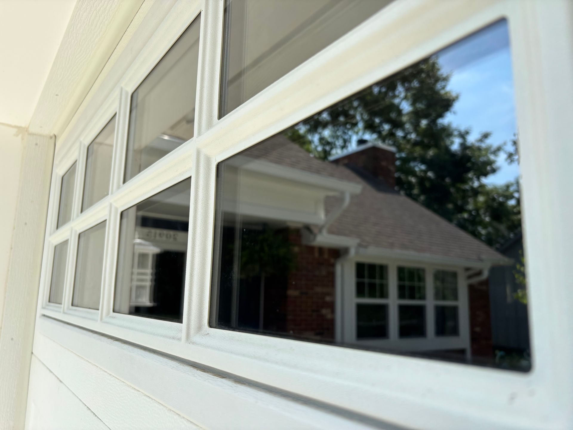 White-framed windows reflect a brick house, trees, and blue sky.