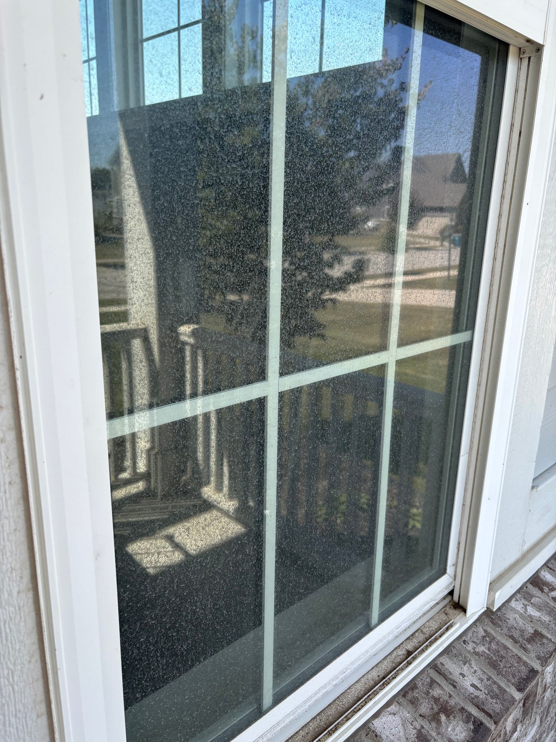 Sliding glass door with white frame is covered in a speckled substance. Door reflects a porch and house across the street.