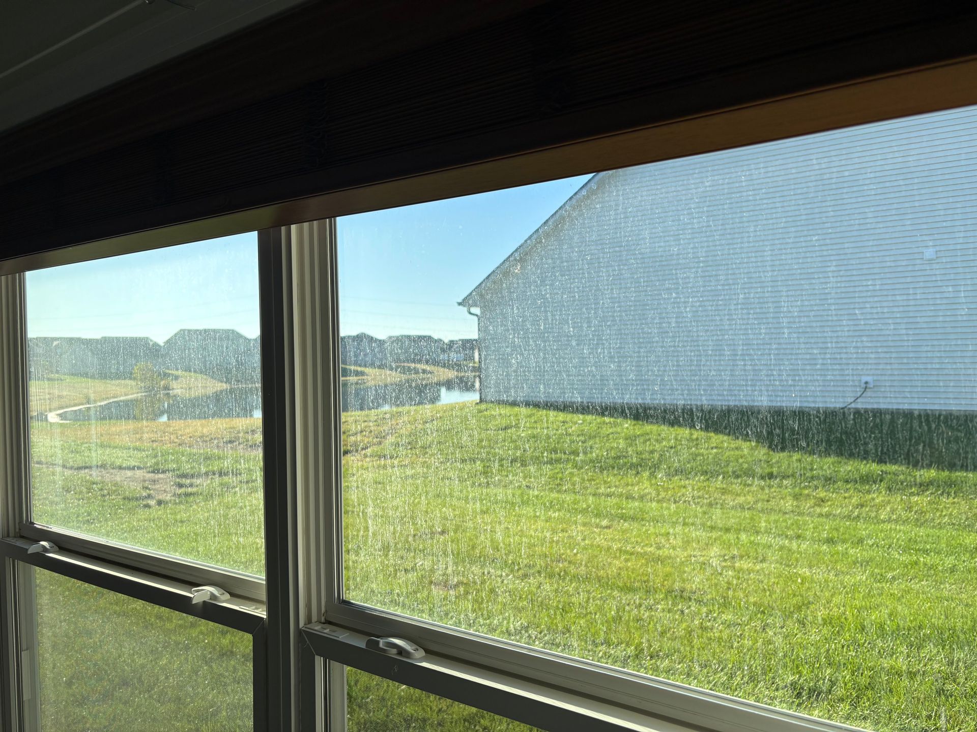 View through a window, showing a green lawn, lake, and white house under a blue sky.