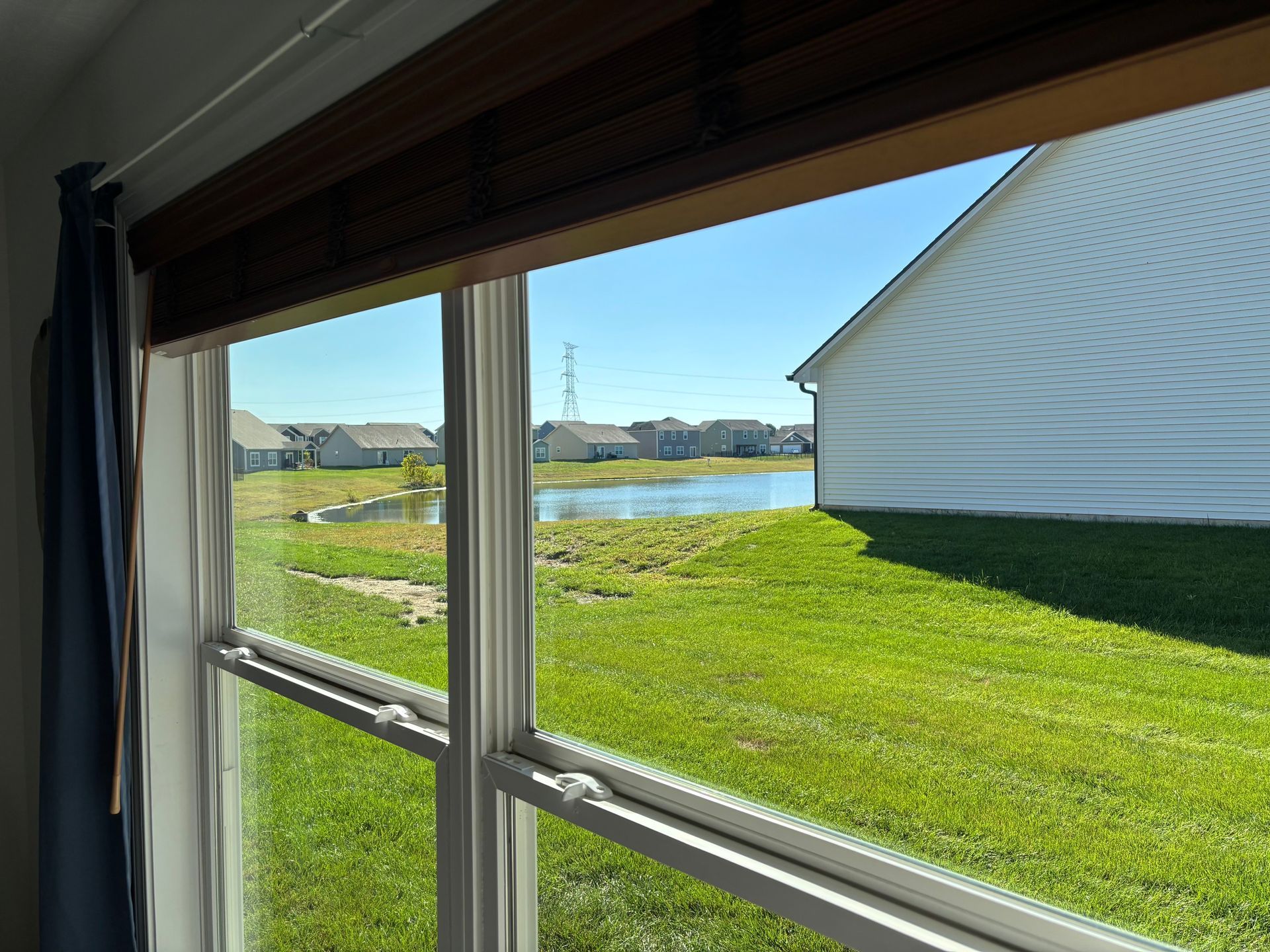 View through a window of a grassy yard with a pond and houses on a sunny day.