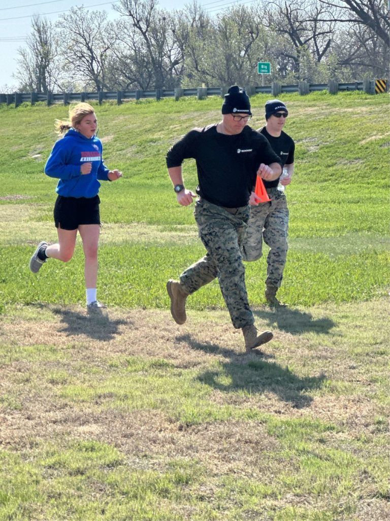 Three runners jogging on a grassy field on a sunny day