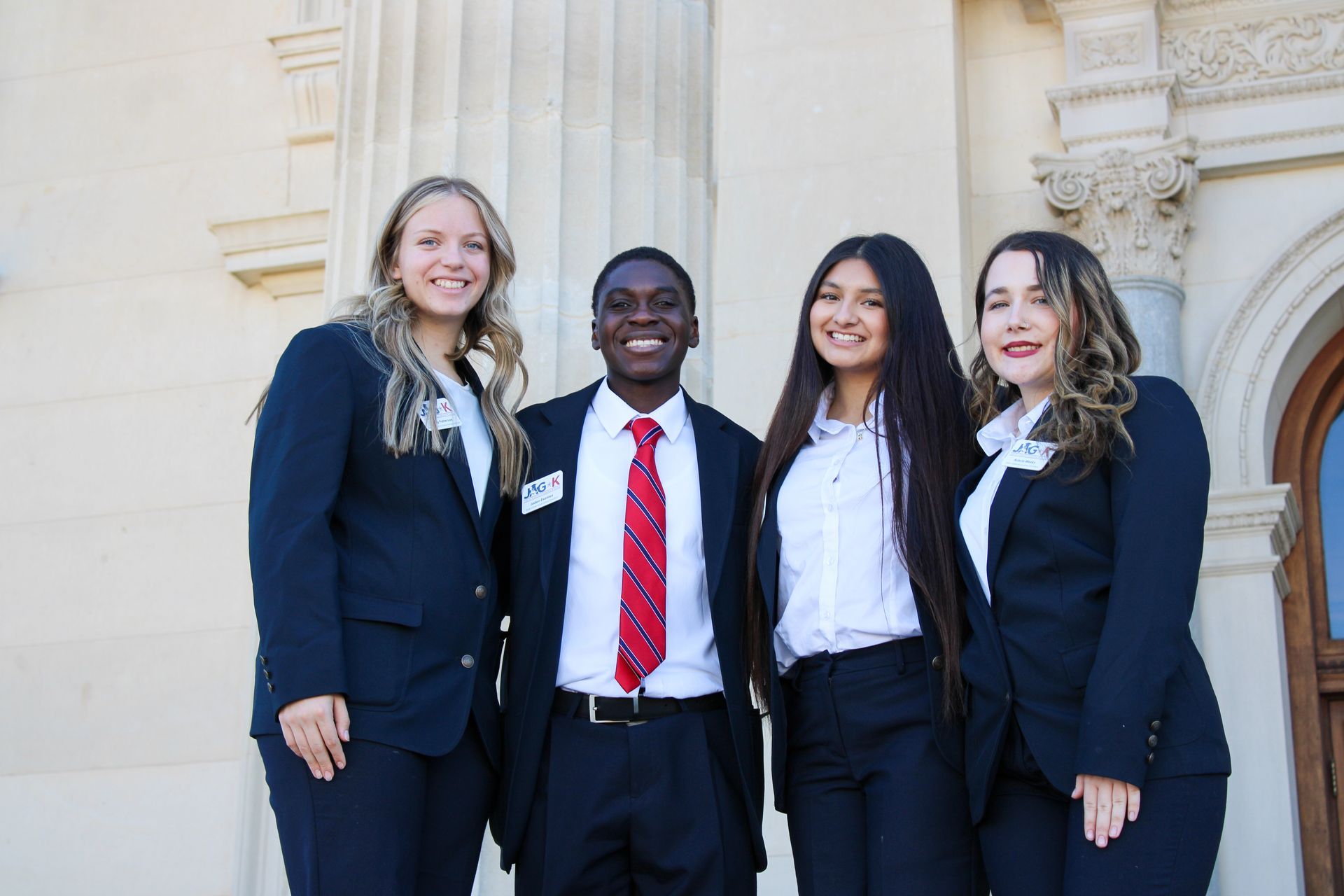 Four professionally dressed people standing together outside a building, smiling at the camera.
