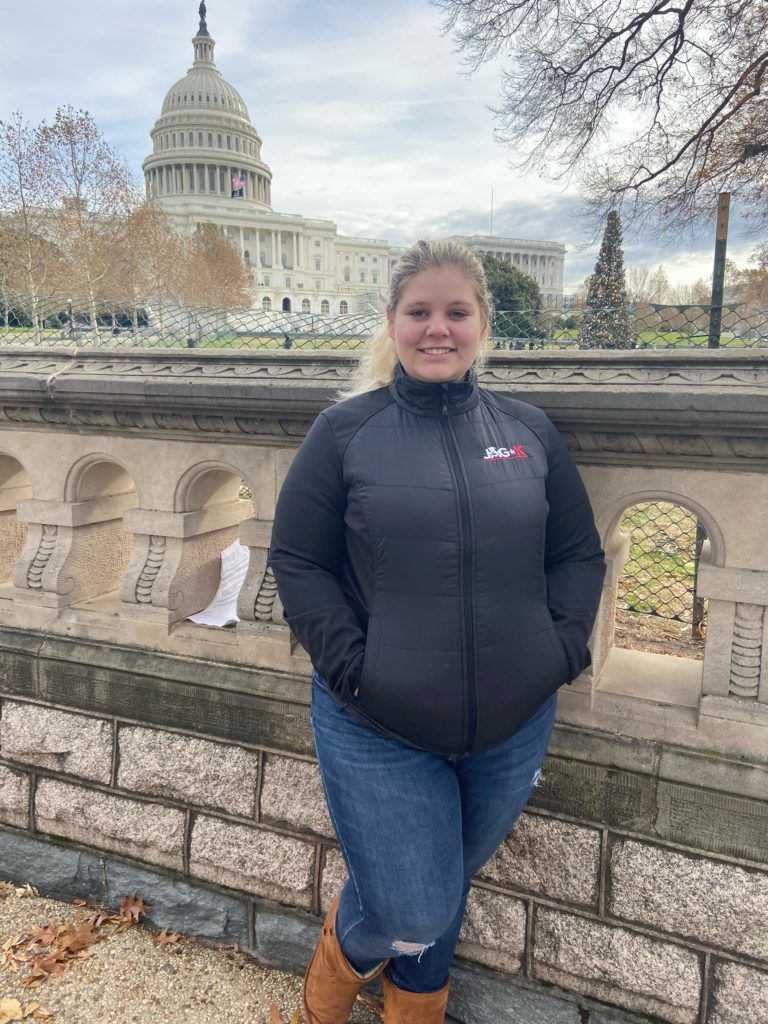 Person standing by a stone railing with the U.S. Capitol in the background.