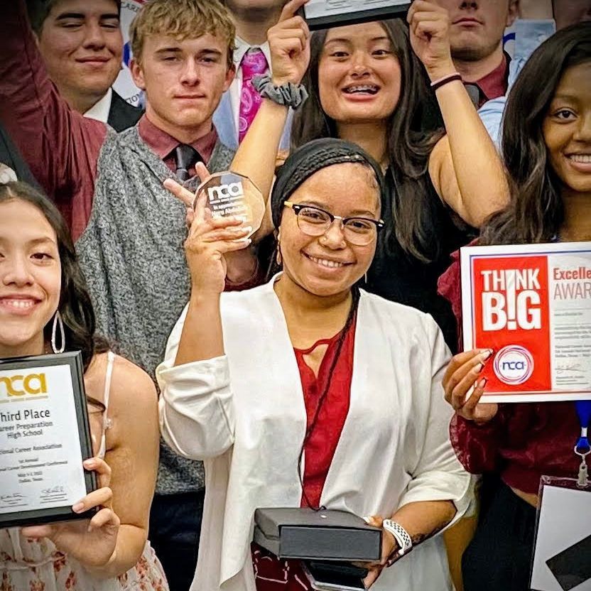 Group of students smiling and holding awards, one raising a trophy at a celebration event.