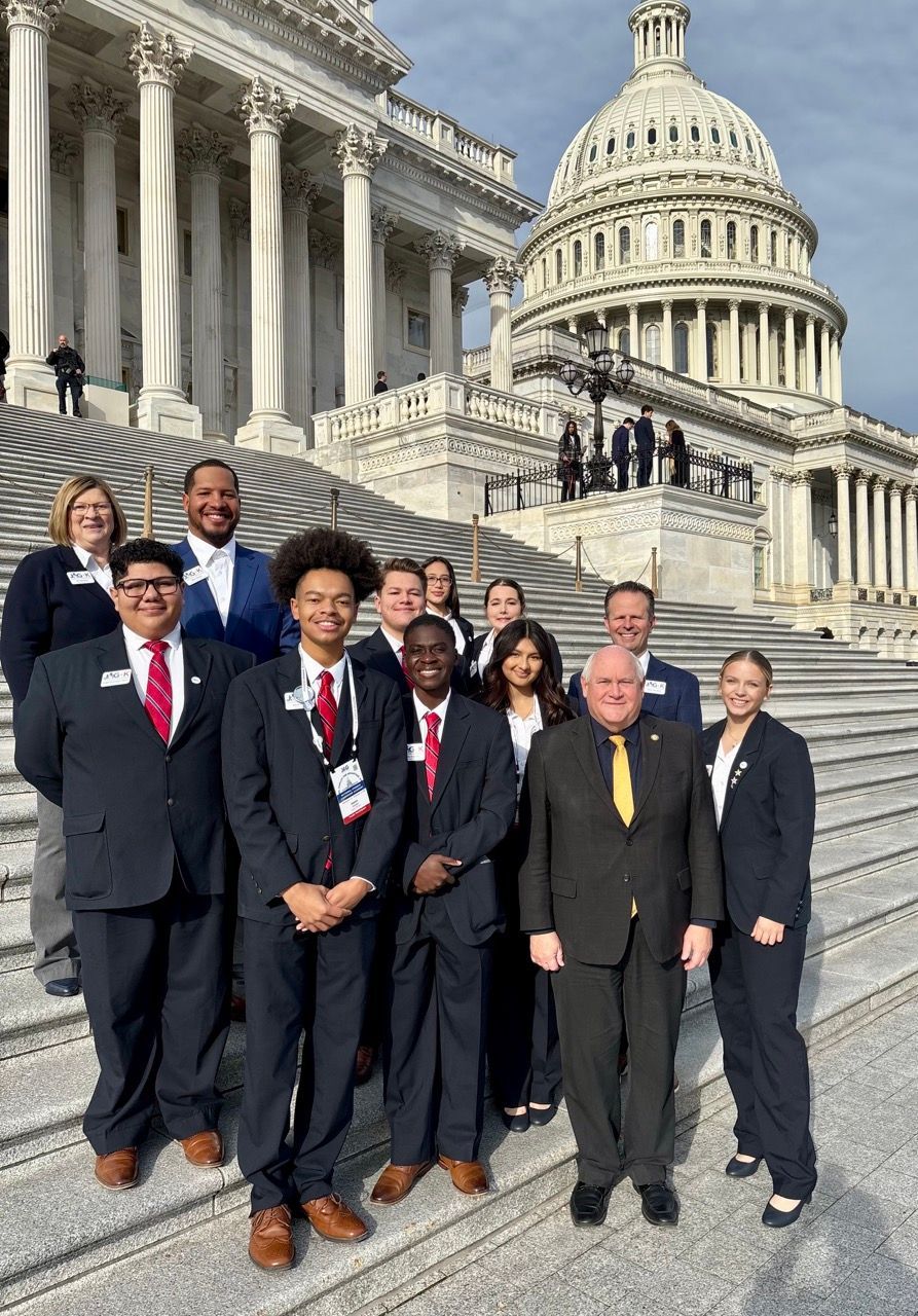 Group of people in suits posing on the Capitol steps in front of the U.S. Capitol building