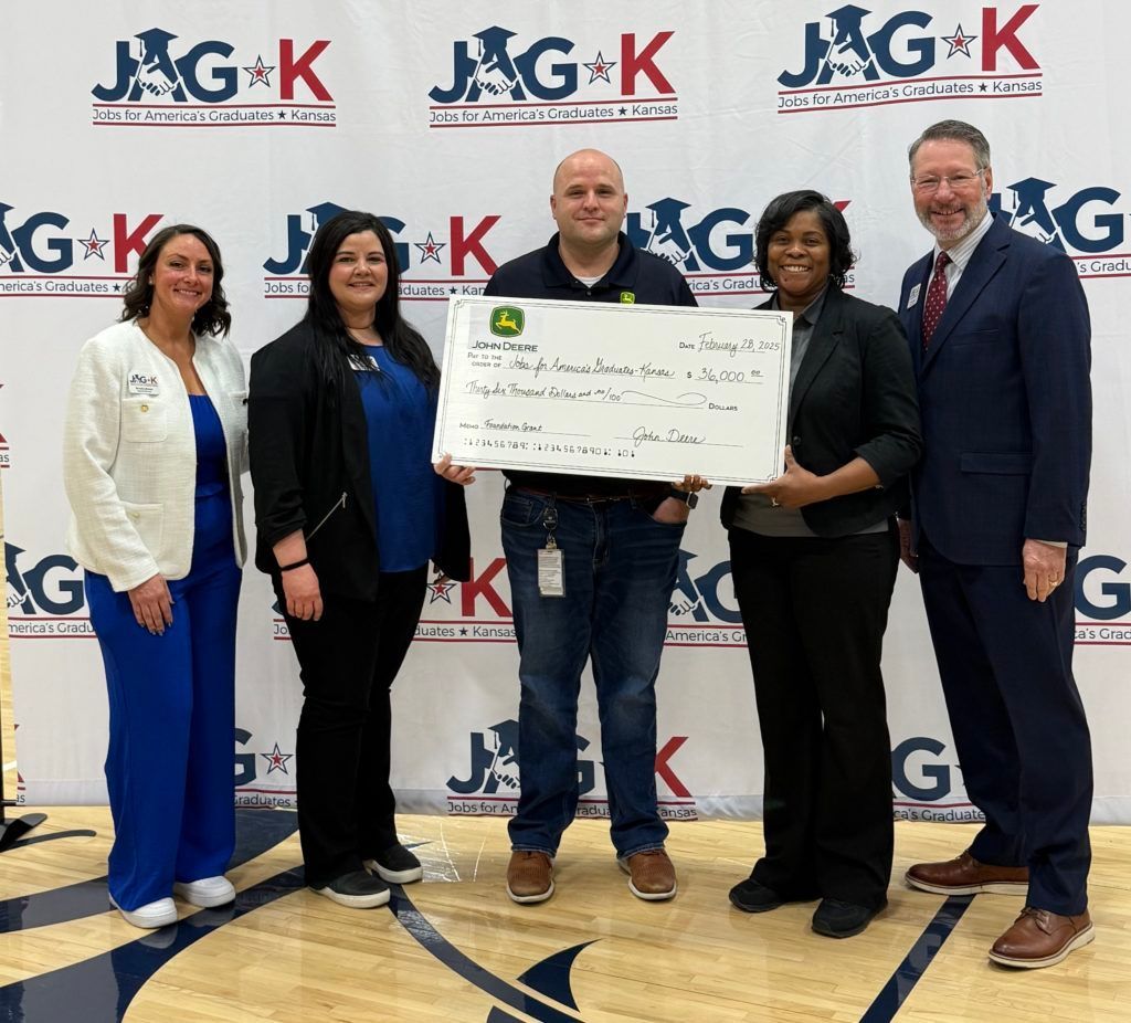 Five people stand on a gym floor holding a large check in front of a J&G K backdrop.