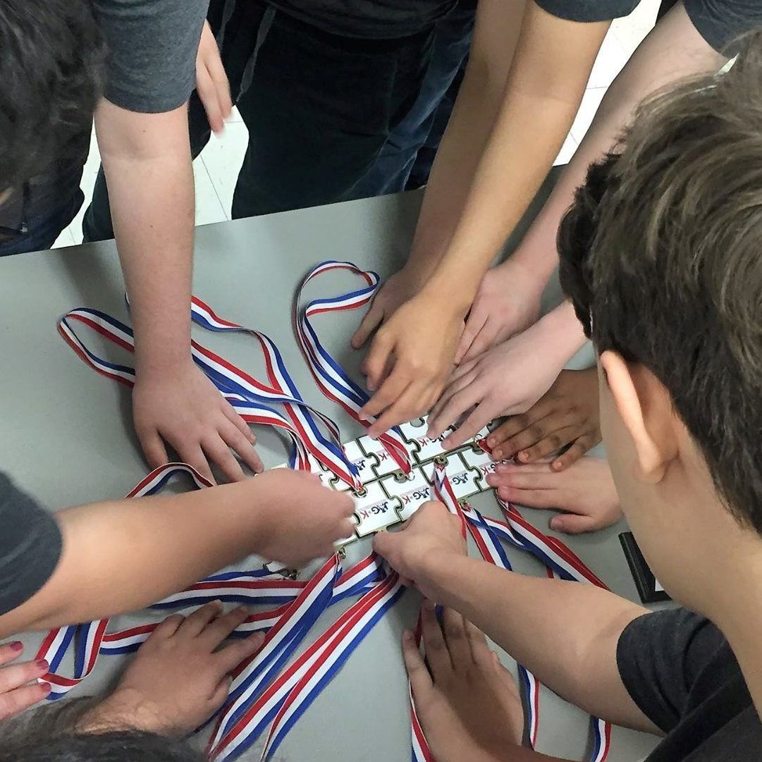 Hands of several people joining together over a table with red, white, and blue ribbons