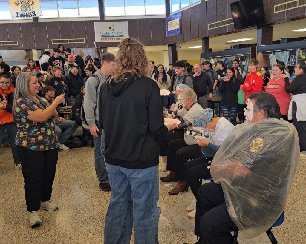 Crowded indoor gathering with people seated and standing in a public cafeteria or hall