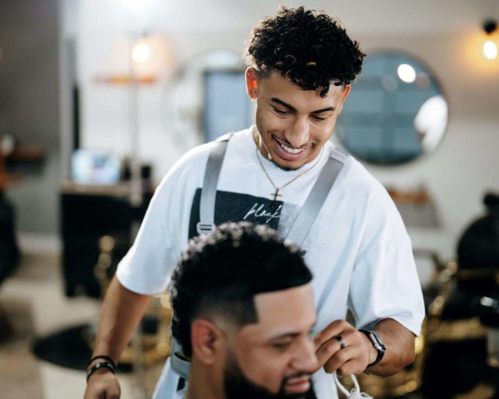 Barber styling a client’s hair in a bright barbershop, both smiling