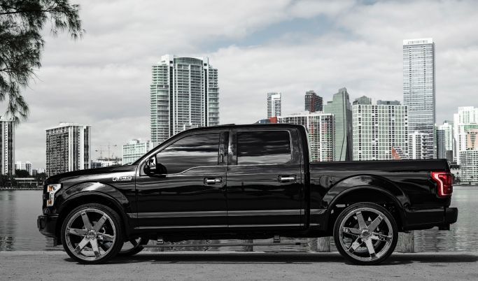 A black pickup truck is parked on the side of the road in front of a city skyline.