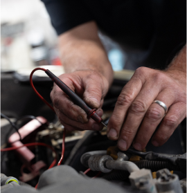 A person is working on a car battery with a red cable | All-Star Automotive