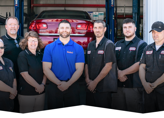 A group of people standing in front of a red car on a lift | All-Star Automotive